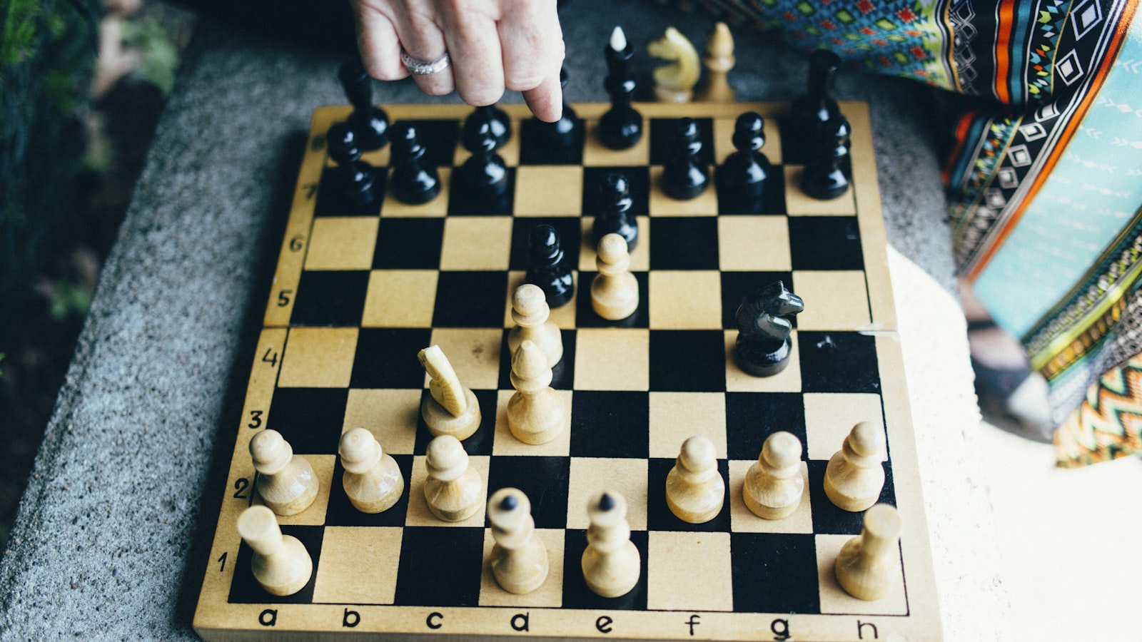 A hand reaching down to move a piece on a wooden chessboard