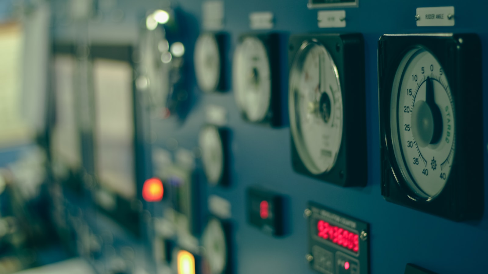 A shallow-focus row of analog gauges, indicator lights, and controls on an industrial panel