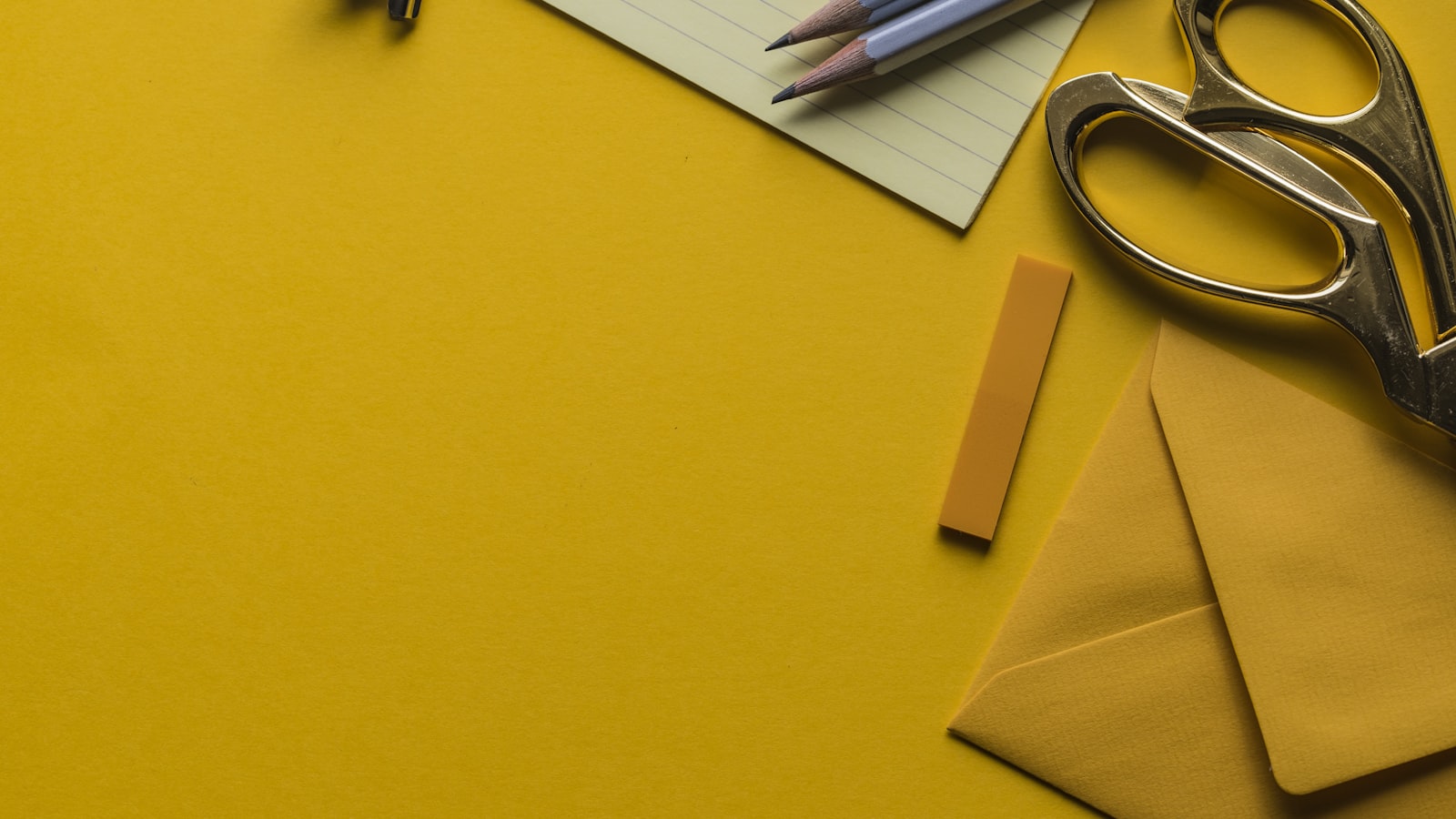 A flat-lay of office supplies — scissors, pencils, and a notepad on a yellow background