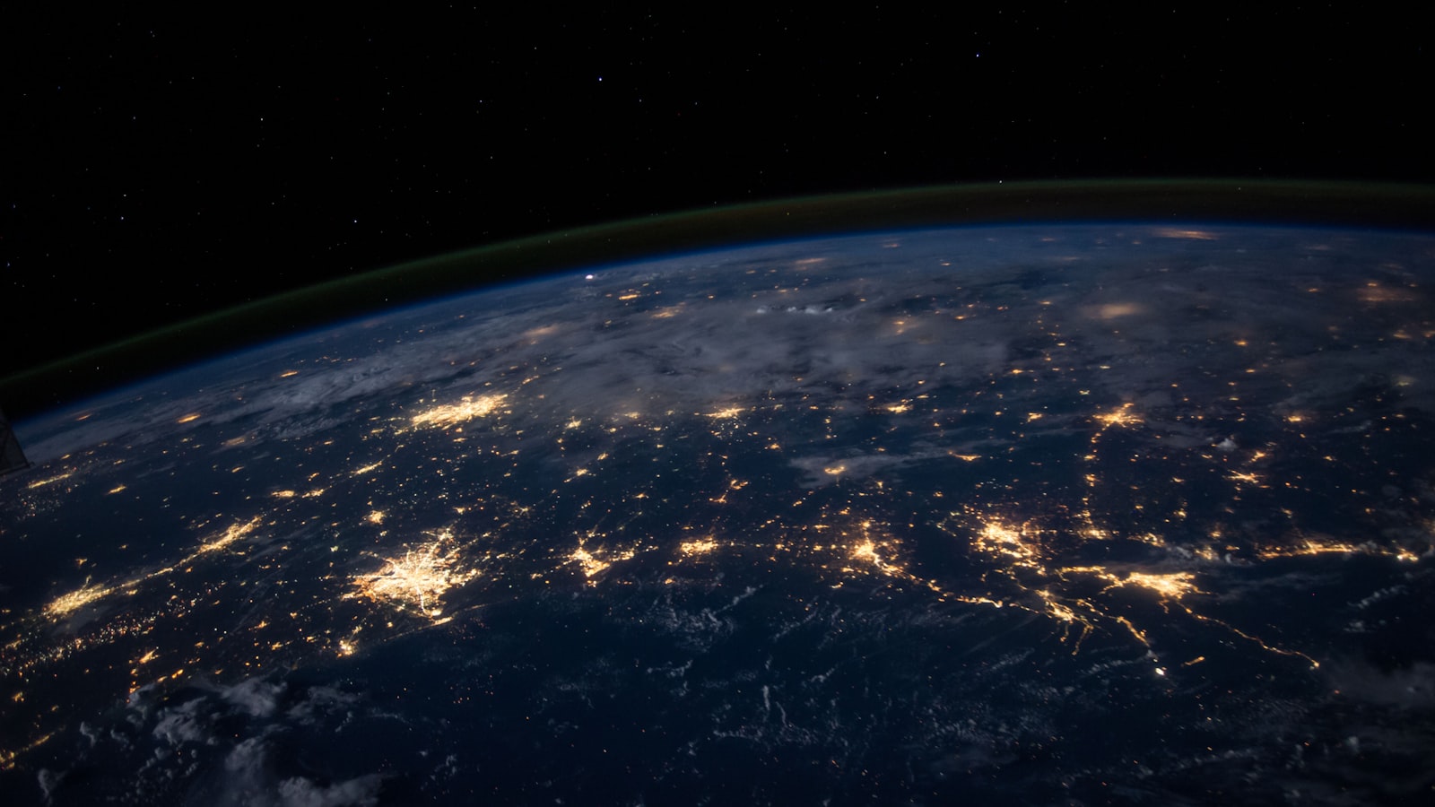 Earth seen from orbit at night, with city lights traced across continents