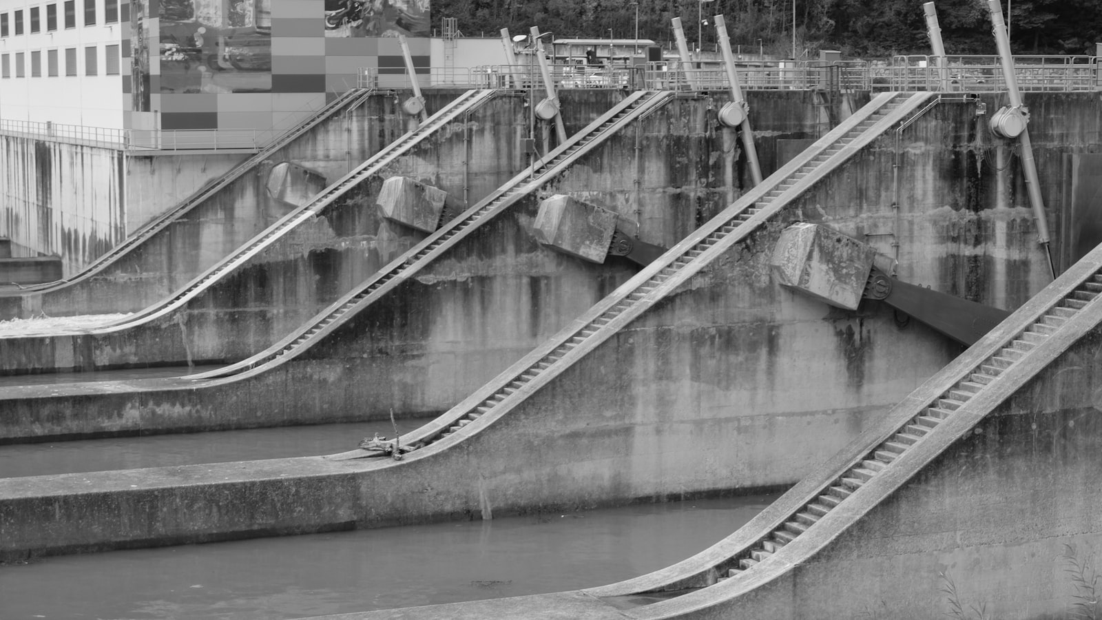 Concrete spillway channels of a dam stepping down toward calm water