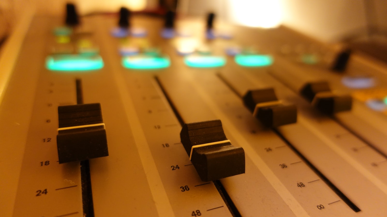 A close-up of a sound mixing console with rows of knobs, buttons, and faders